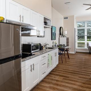 A modern apartment kitchen with an open layout, featuring stainless steel appliances, white cabinets, and hardwood flooring.