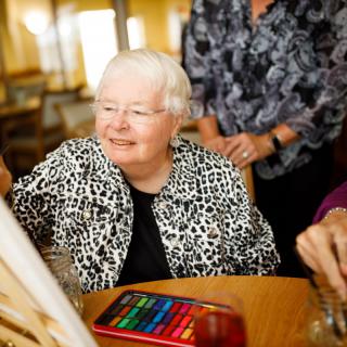 An elderly woman smiles as she participates in a painting activity with others.