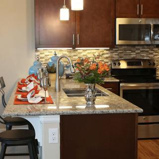 A modern kitchen interior featuring a central island with stools and stainless steel appliances.