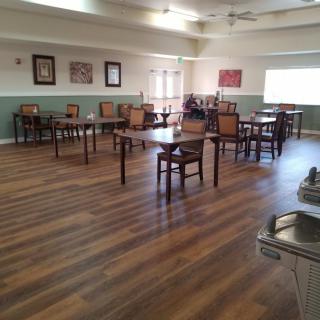 An empty dining room with wooden floors, featuring tables and chairs, and a ceiling fan overhead.