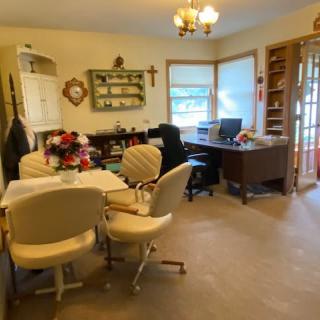 A cozy home office with a desk, bookshelf, and chairs arranged around a table, accented by natural light from the window.