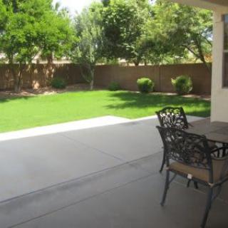 A view of a backyard with a patio, lawn, and outdoor furniture.