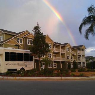 A rainbow arches over an apartment building with a bus parked in front.