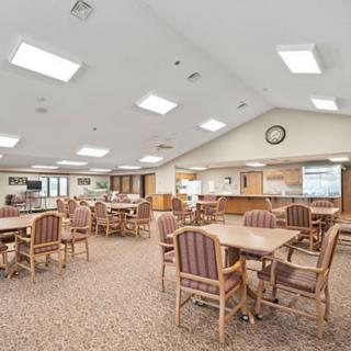 A spacious dining area with multiple tables and chairs, featuring bright overhead lighting and a carpeted floor.