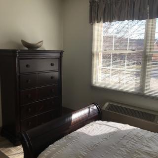 A sunny bedroom with a bed, dresser, and large window.