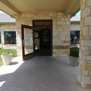The entrance of a stone building with an open door, featuring outdoor potted plants.