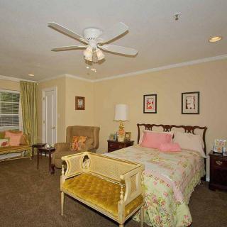 A cozy bedroom featuring a bed with decorative pillows, an armchair by the window, and a ceiling fan overhead.