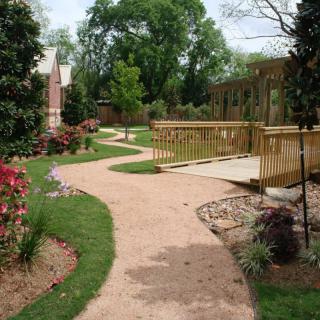 A serene garden with a winding pathway and wooden bridge, surrounded by lush greenery.