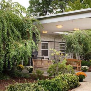 A cozy porch surrounded by lush greenery and vibrant flowers.