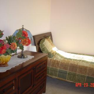 A cozy bedroom with a single bed and a dresser decorated with flowers.