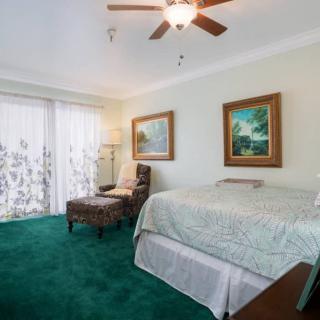 A cozy bedroom with a green carpet, featuring a bed, paintings on the wall, and a ceiling fan.