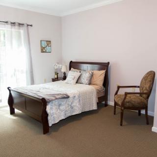 A cozy bedroom featuring a wooden bed, elegant chair, and soft curtains.