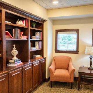 A cozy reading nook with a wooden bookshelf, comfortable armchair, and a window allowing natural light in.