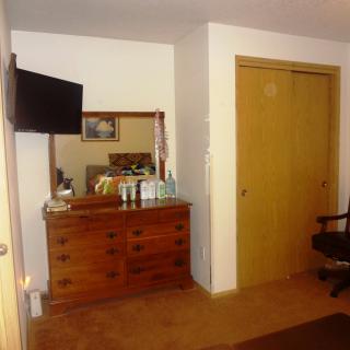 A cozy bedroom featuring a wooden dresser with a mirror, a wall-mounted television, and a closet.