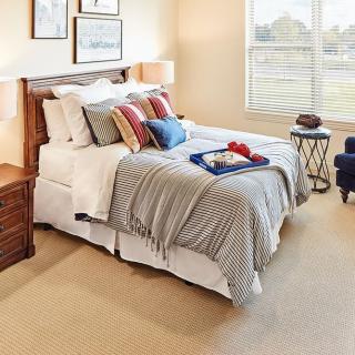 A cozy bedroom with a neatly made bed, pillows, and a bedside table with a lamp.