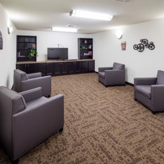 A lounge area featuring several gray armchairs, a television, and carpeted flooring.