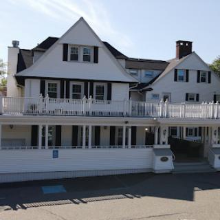 A charming two-story white house with a spacious deck, showcasing classic architectural features.