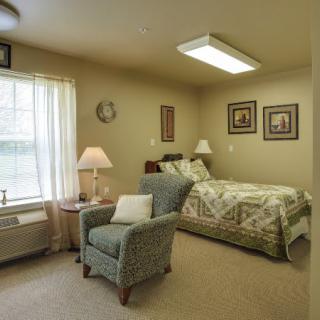 A cozy bedroom with a bed, armchair, lamp, and window with curtains.