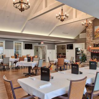 A cozy restaurant interior featuring a dining area with neatly arranged tables and chairs, chandeliers, and a fireplace.