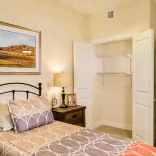 A cozy bedroom with a neatly made bed, an open closet, and warm lighting from a bedside lamp.