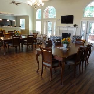 A well-lit dining area with multiple tables and chairs, featuring wood flooring and large windows.