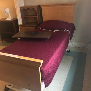 A hospital bed with a burgundy cover and an adjustable side table in a room.