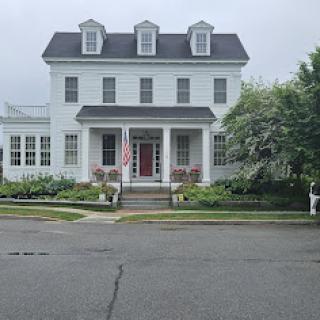 A charming two-story white house with a welcoming front porch and a beautifully landscaped garden.