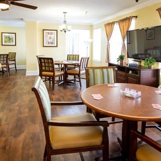 A cozy dining area with wooden tables and chairs, featuring ceiling fans and natural light from large windows.