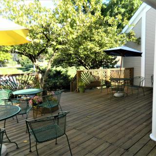 A sunny backyard deck with outdoor seating and umbrellas surrounded by greenery.