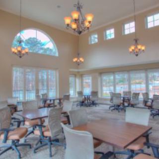 A spacious dining area with large windows, multiple tables and chairs, and elegant chandeliers.