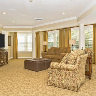 A cozy living room with patterned furniture, a large TV, and ample natural light from multiple windows.