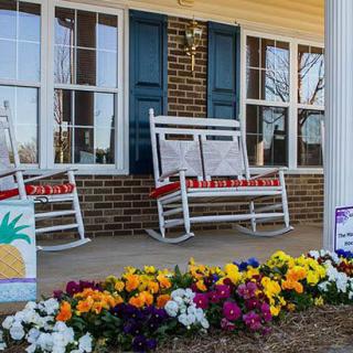 A cozy front porch with white rocking chairs and vibrant flowers.