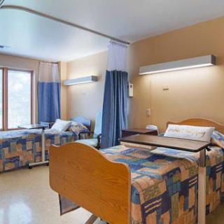 A spacious and well-lit hospital room with two beds and privacy curtains.