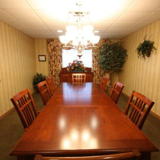 A well-lit dining room with a long wooden table, surrounded by chairs and decorated with indoor plants.