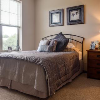 A cozy bedroom with a neatly made bed, soft lighting, and decorative framed pictures on the wall.