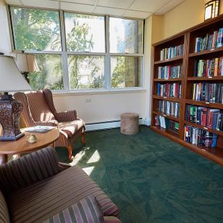 A cozy reading room with a bookshelf, chairs, and natural light.