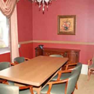 A dining room with a wooden conference table surrounded by green chairs, featuring red walls, a painting, and a chandelier.