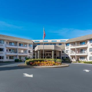 A hotel entrance with a circular driveway and manicured landscaping, featuring a flag in front.