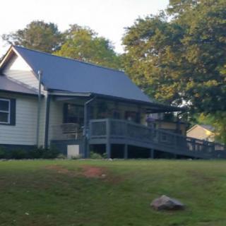 A cozy house with a porch, surrounded by trees and a grassy lawn under the sunlight.