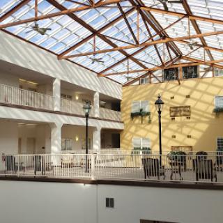 A spacious atrium featuring a glass roof and wooden beams, designed with balconies and seating areas.