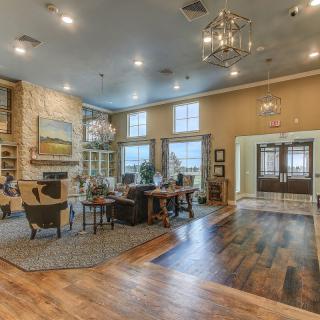 A spacious and cozy living room with wood flooring, elegant chandeliers, and a warm fireplace.