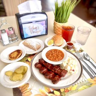 A delicious breakfast spread featuring various dishes including grilled meat, baked beans, pickles, and a sweet pastry.