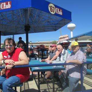 A group of people sitting at a table under an umbrella on a sunny day.