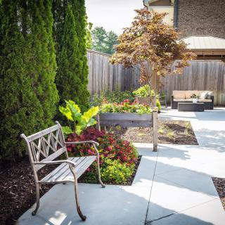 A beautifully landscaped garden with a bench, raised plant beds, and a patio area.