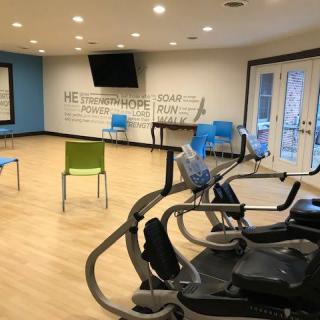 A well-lit gym room with exercise equipment and chairs arranged on a wooden floor.