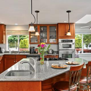 Modern kitchen with granite island and wooden cabinets, featuring pendant lighting and stainless steel appliances.