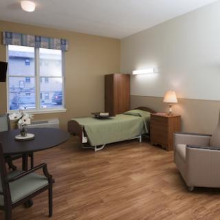 A well-lit hospital patient's room featuring a bed, seating area, and natural light from the window.