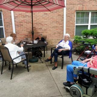 A group of seniors sitting outdoors on a patio, enjoying the day under an umbrella.
