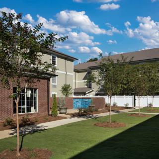 A view of apartment buildings with a well-maintained lawn and trees under a clear sky.