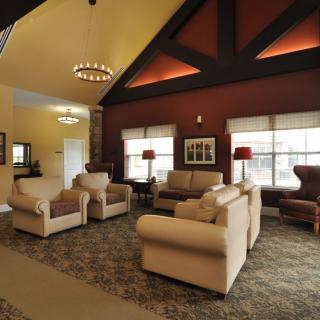 A cozy lobby area with comfortable armchairs and sofas, accented by a chandelier and large windows.